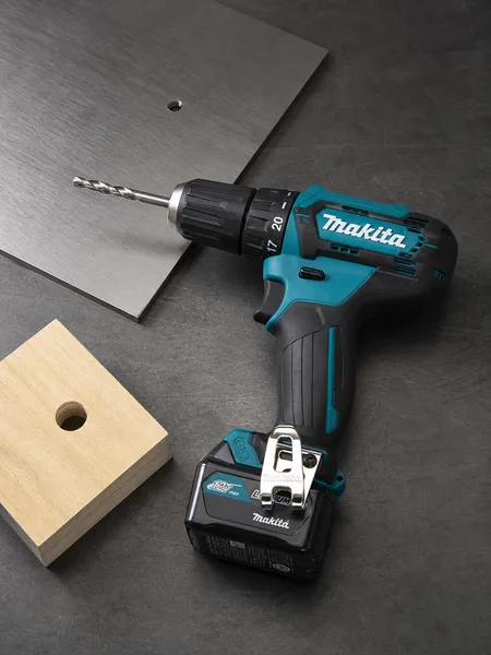 Шуруповёрт Makita рядом со стальным листом и деревянным бруском со сквозными отверстиями